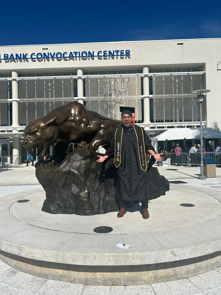 Graduation portrait in cap and gown with a U.S. Army stole, beside the university panther statue