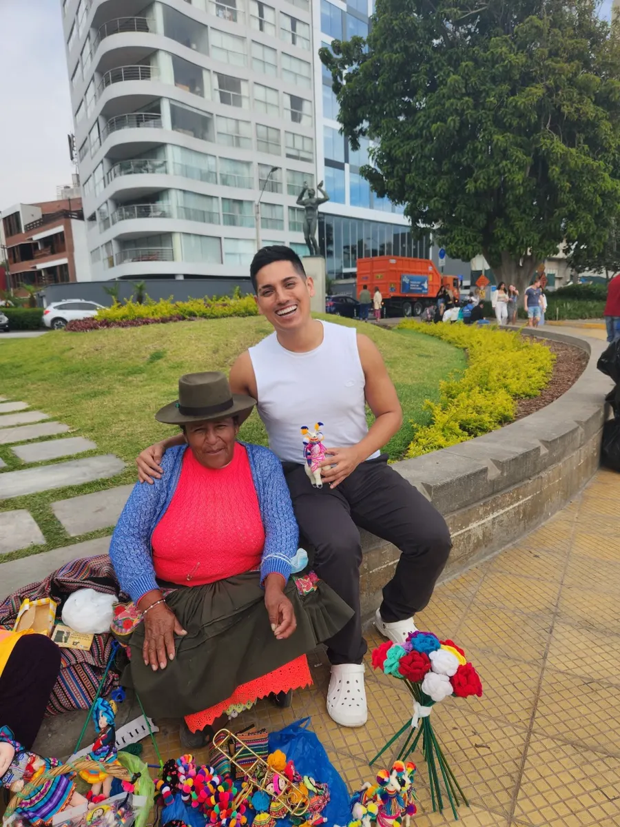 Alvaro seated beside an artisan and her handmade crafts on a seaside promenade